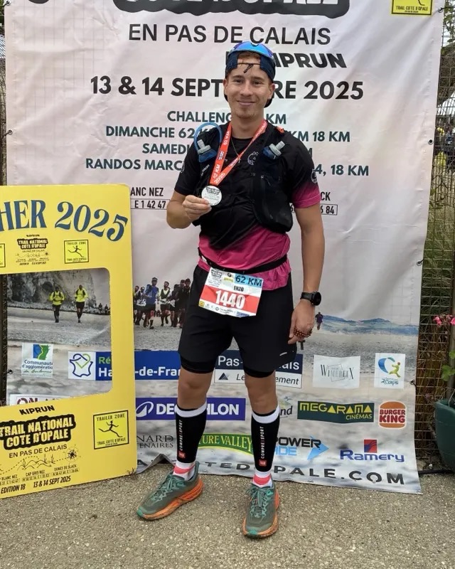 Enzo montre sa médaille de finisher devant l'affiche du Trail Côte d'Opale